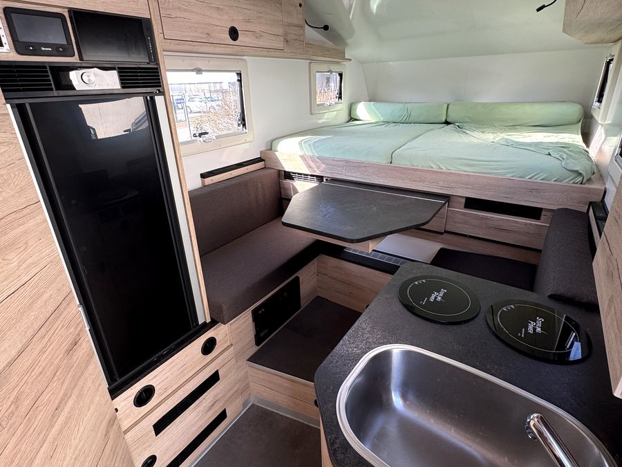 Küche mit Spüle und Kochfeld in der Wohnkabine, dahinter das Bett